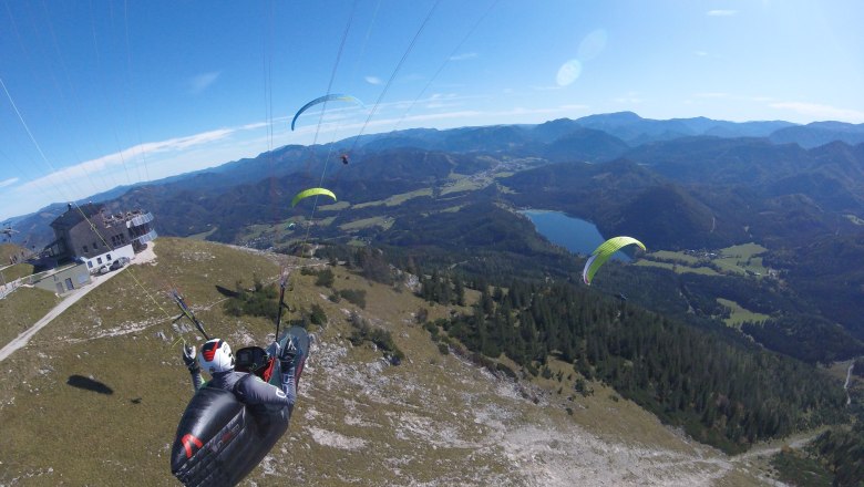 Paragleiter auf der Gemeindealpe, © Wolfgang Schrank Mehrere Gleitschirmflieger über einem Berg mit Blick auf ein Tal und den Erlaufsee