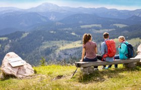 3 Personen sitzen auf Bank und sehen auf das Bergpanorama
