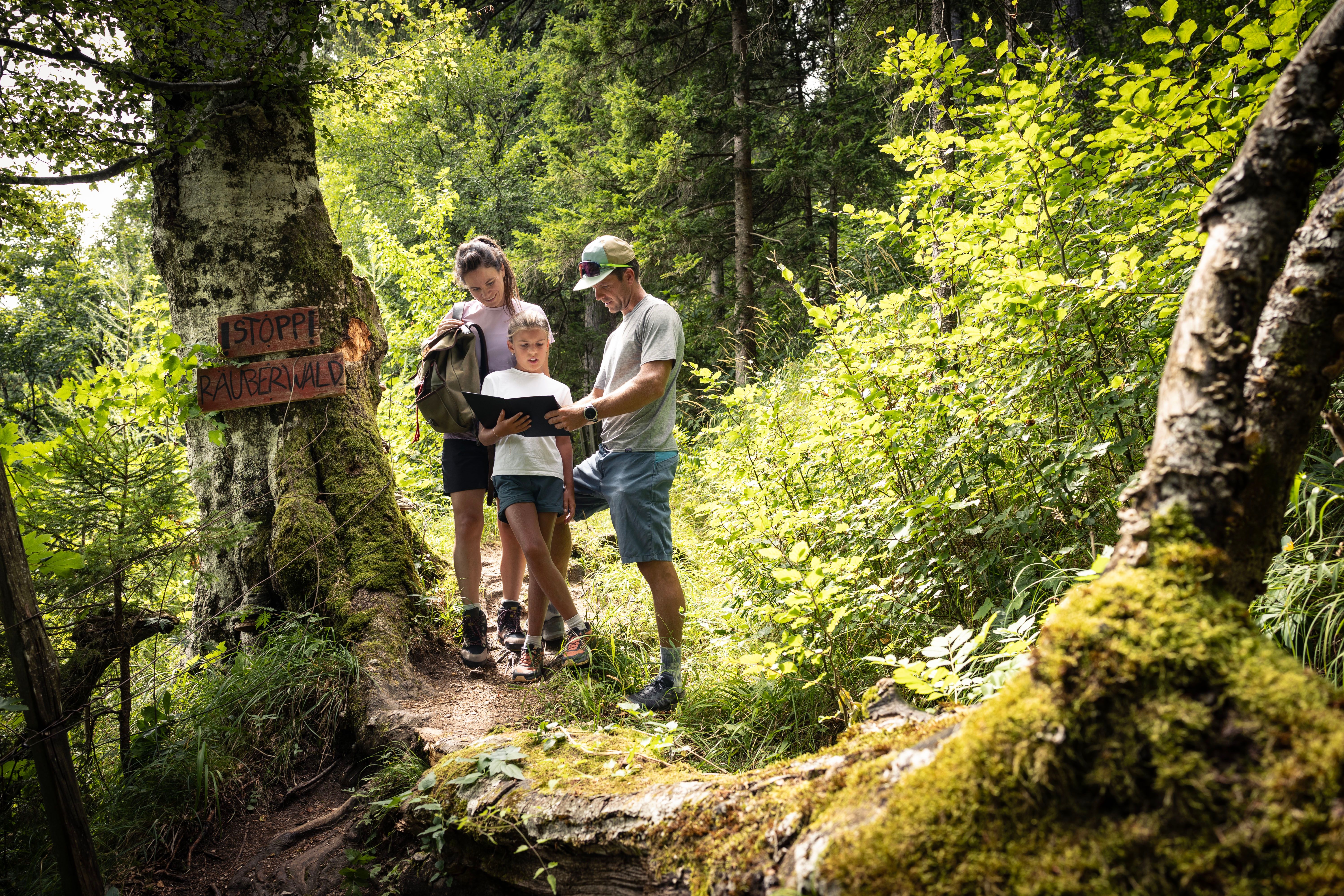 Familie liest gemeinsam eine Rätselmappe neben dem Schild „Stopp! Räuberwald“.