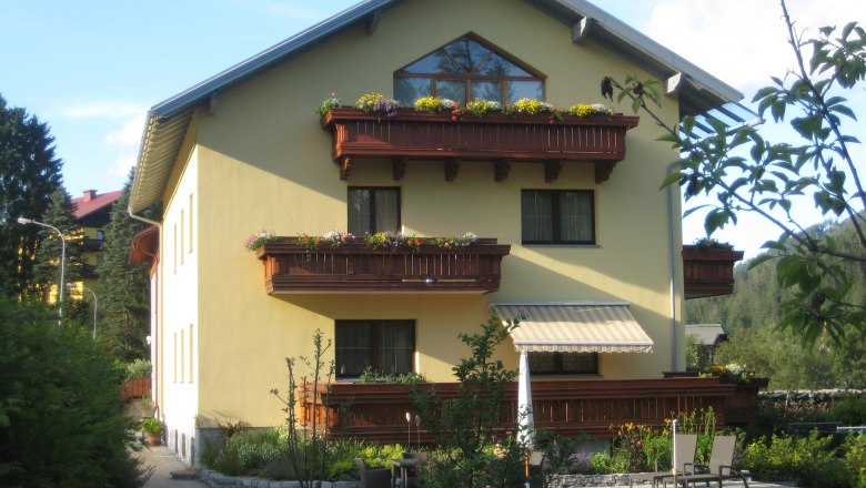 Gelbes Haus mit Holzbalkonen und Garten.