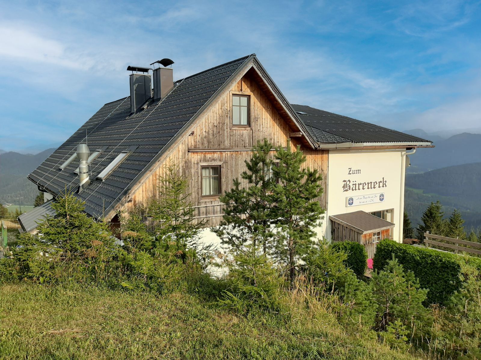 Berggasthaus „Zum Bäreneck“ mit Holzfassade, umgeben von Nadelbäumen und Bergen.