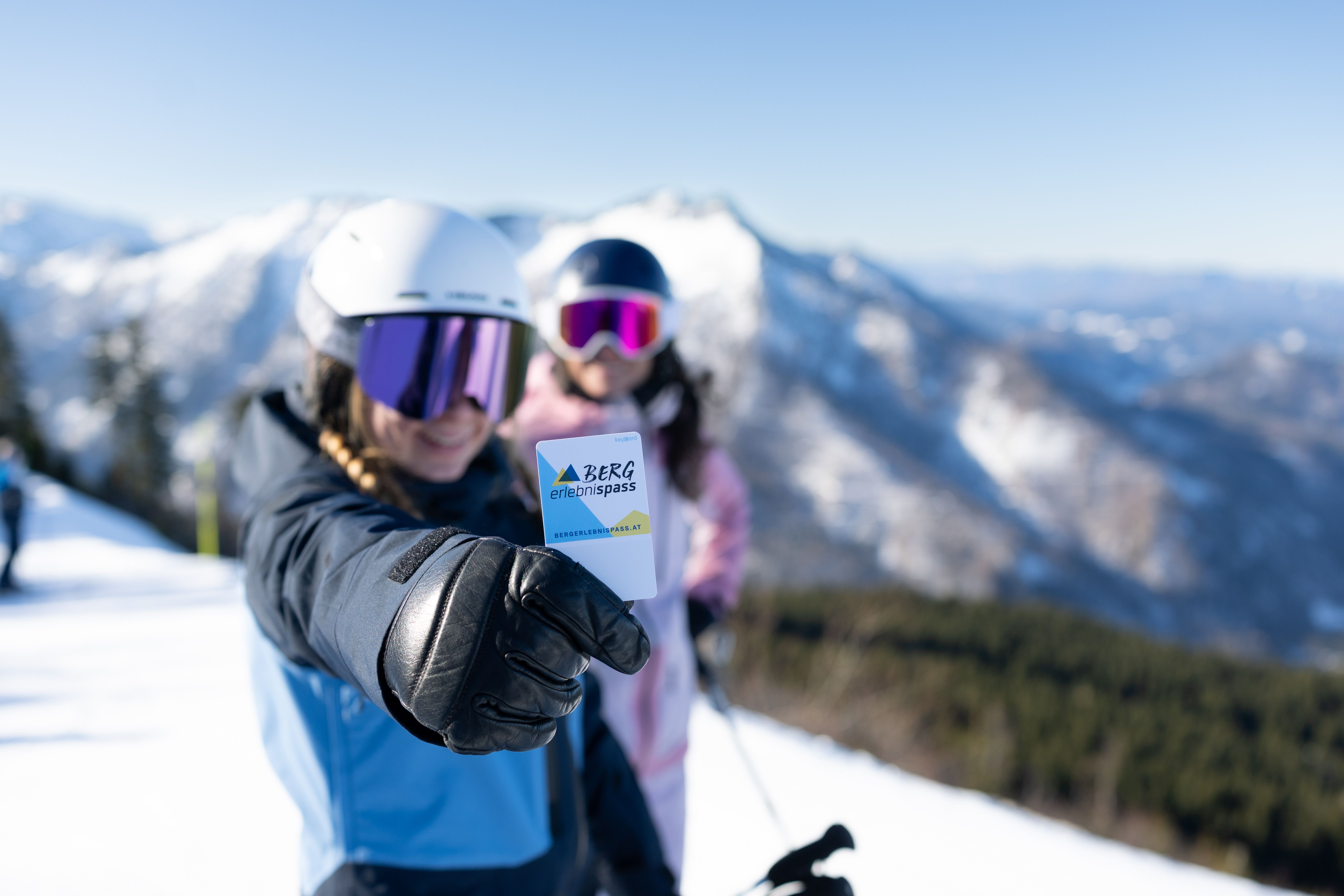 Zwei Skifahrerinnen in Lackenhof am Ötscher; die vordere hält einen Bergerlebnispass in die Kamera.