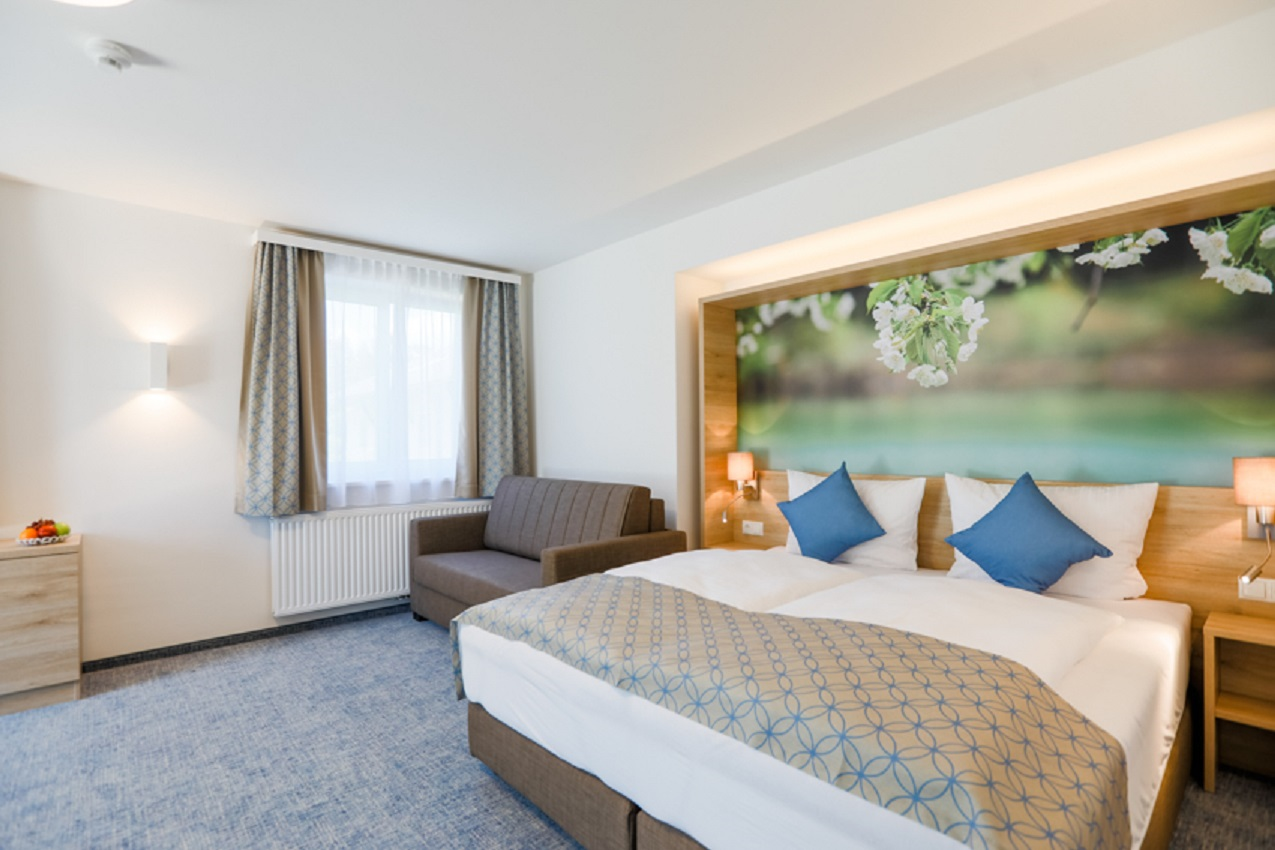 Modernes Hotelzimmer mit Doppelbett, Sofa und großem Wandbild mit Blumenmotiv.