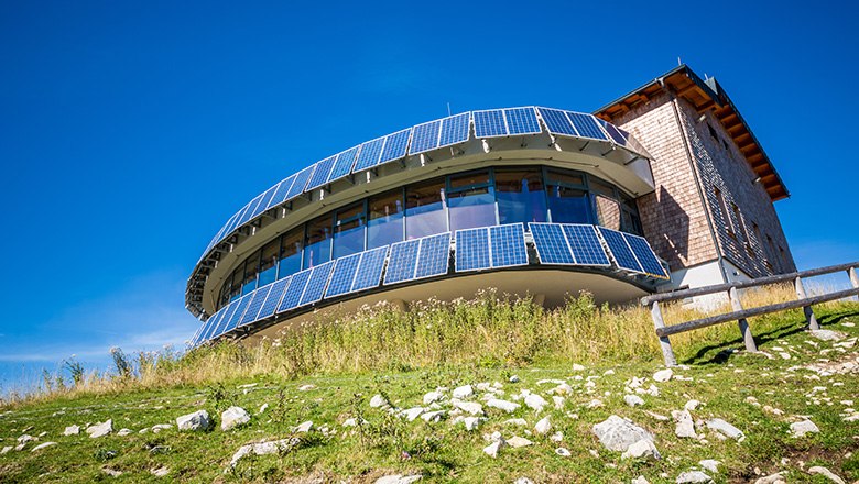 Panoramarestaurant Terzerhaus auf der Gemeindealpe Mitterbach mit moderner Glasfassade und Solarpaneelen, umgeben von Almwiese unter blauem Himmel.