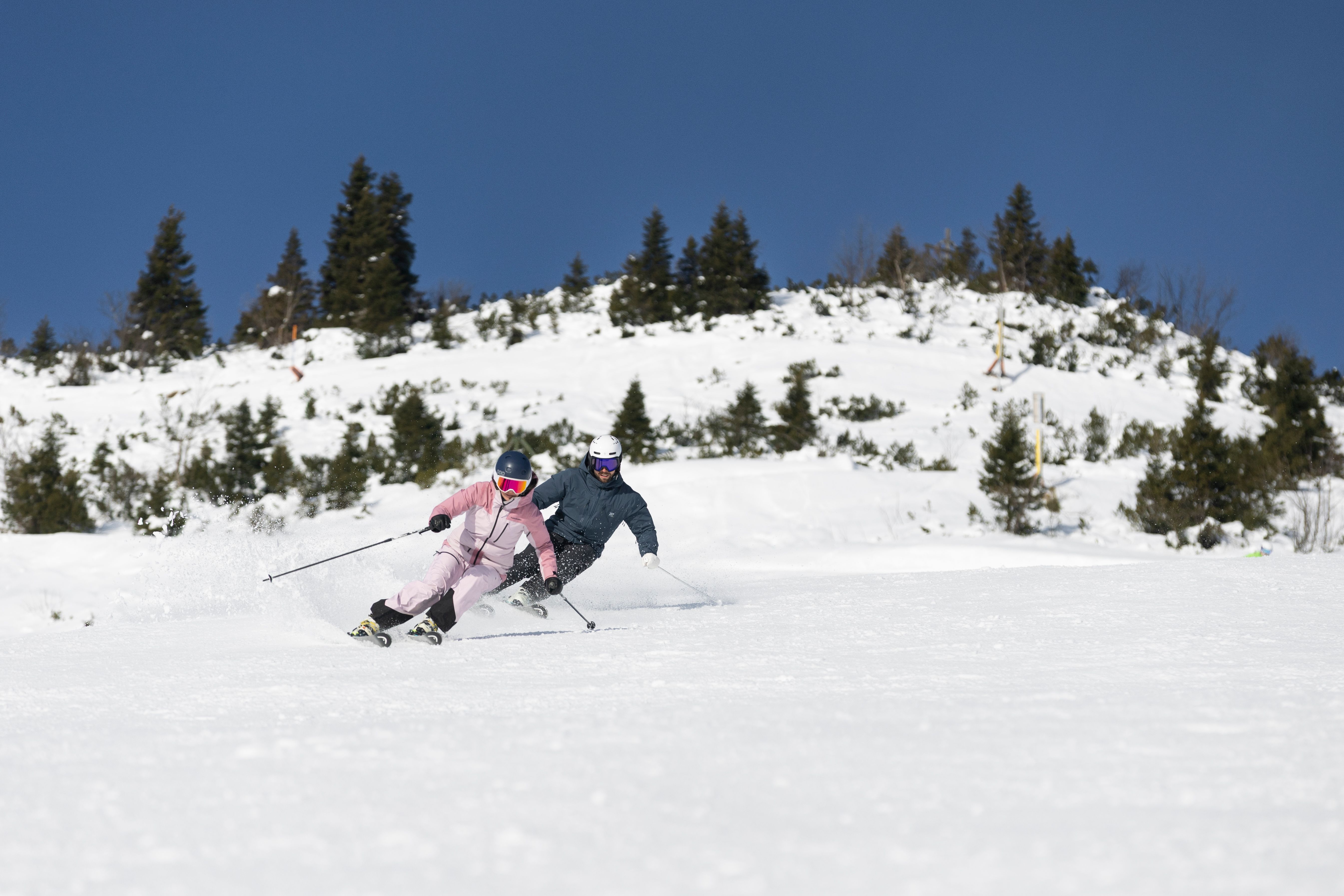 Zwei Skifahrende ziehen auf einer breiten Piste parallel durch den Schnee.
