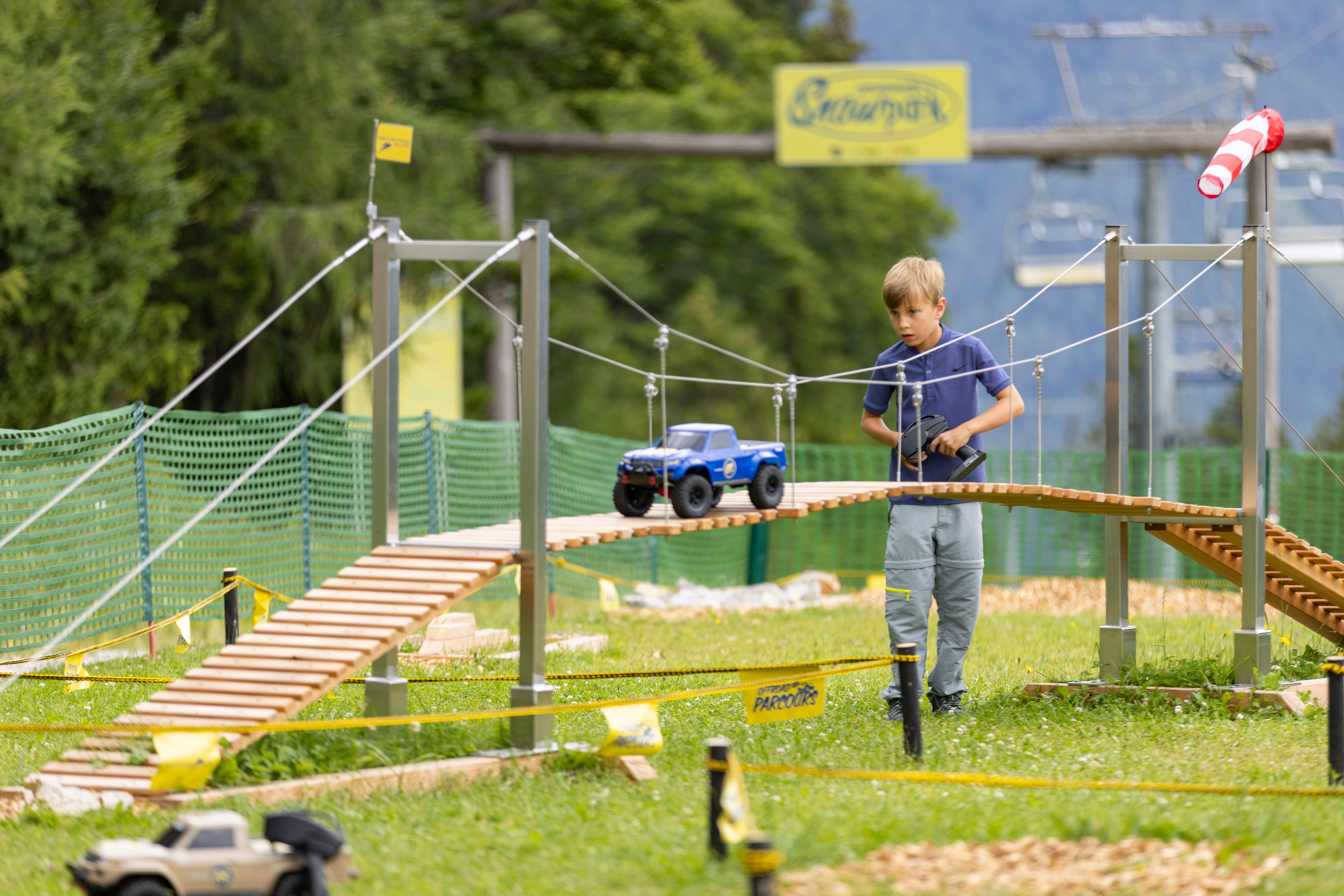 Junge steuert ein ferngelenktes Modellauto über eine hölzerne Hängebrücke.