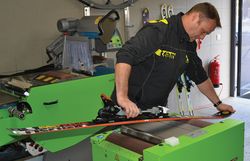 Mitarbeiter bearbeitet einen Ski mit einer Servicemaschine in einer Werkstatt.