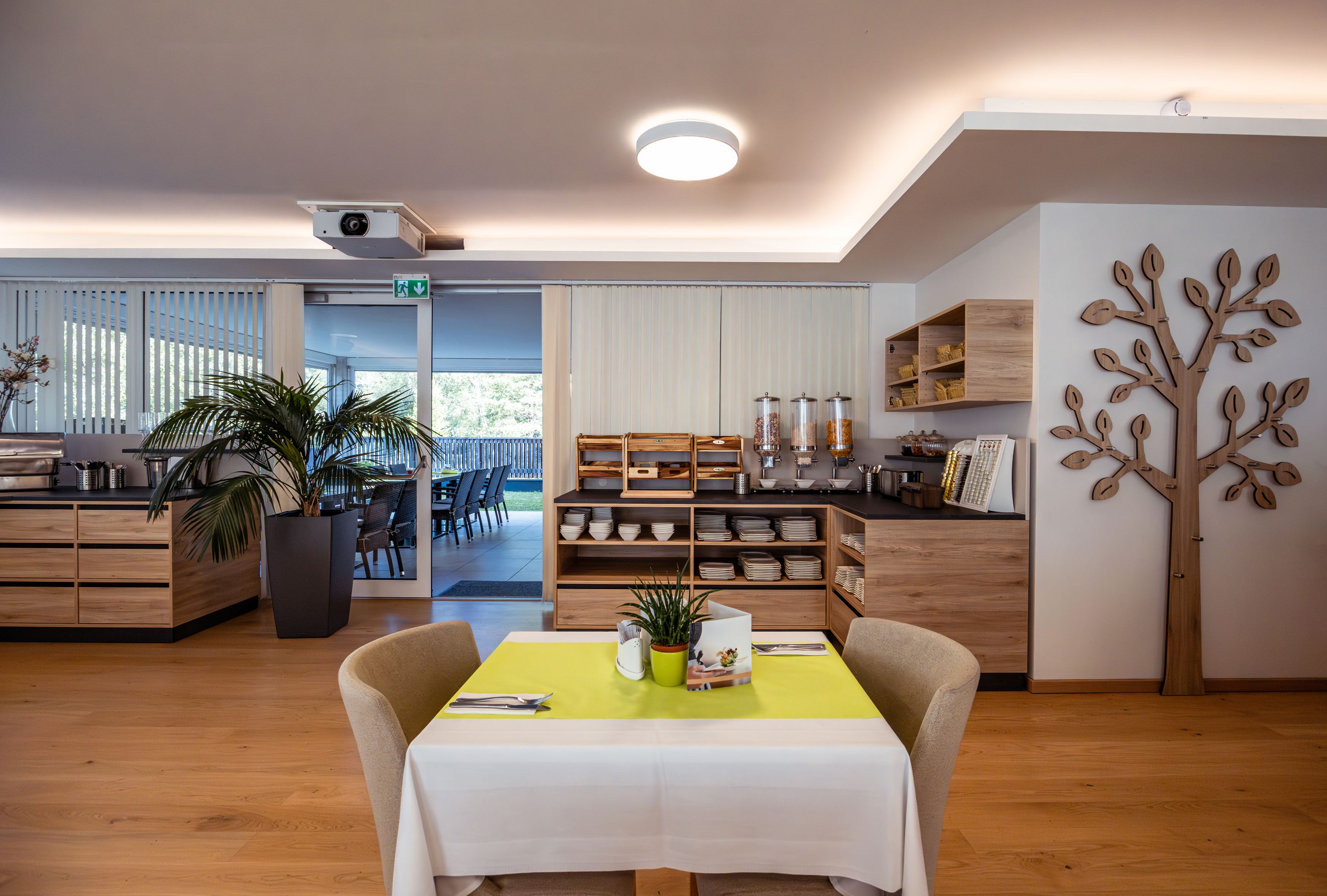 Innenansicht eines Hotelrestaurants mit Frühstücksbuffet und dekorativem Holzelement an der Wand.