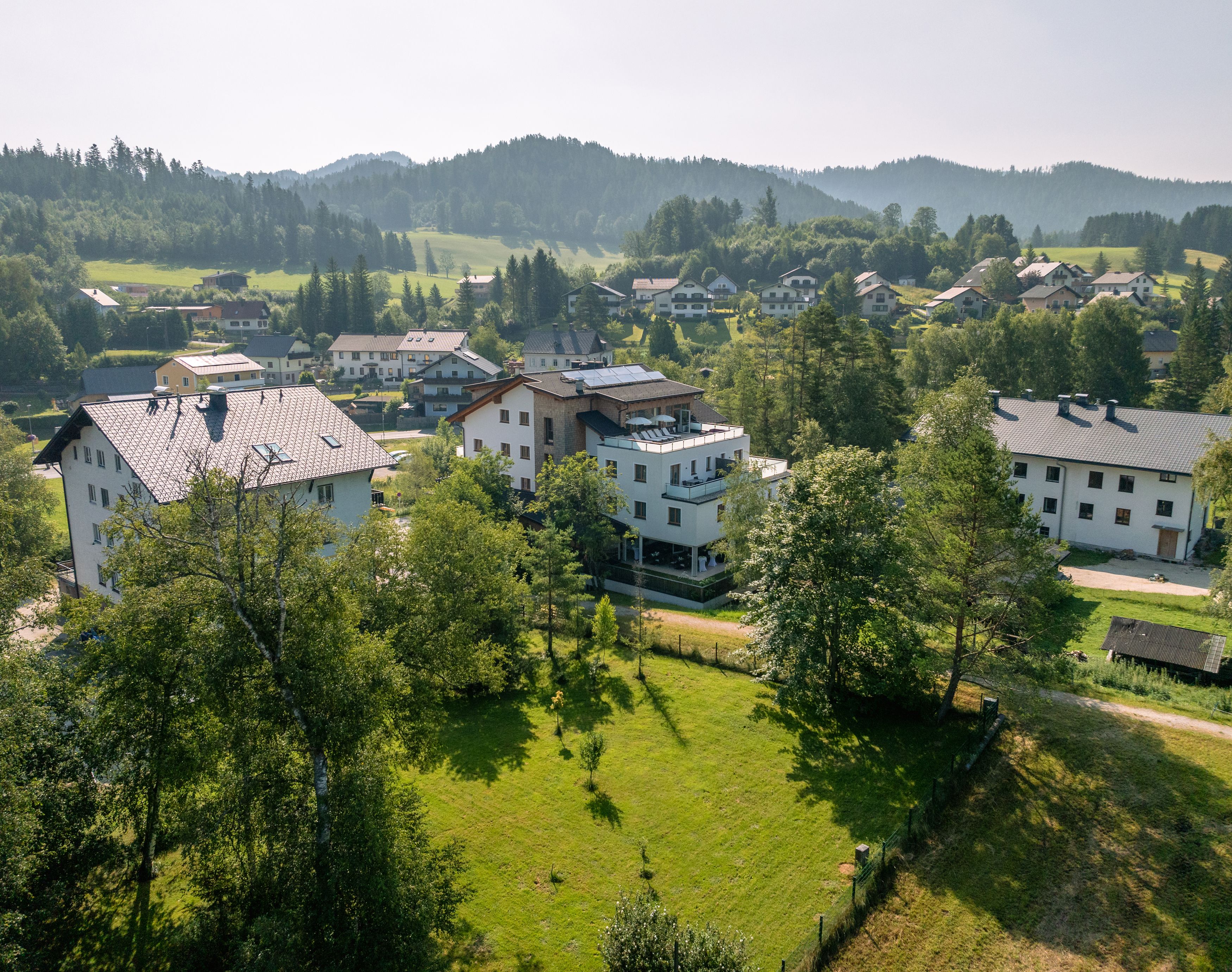 Luftaufnahme von Gebäuden in einer grünen, hügeligen Landschaft.