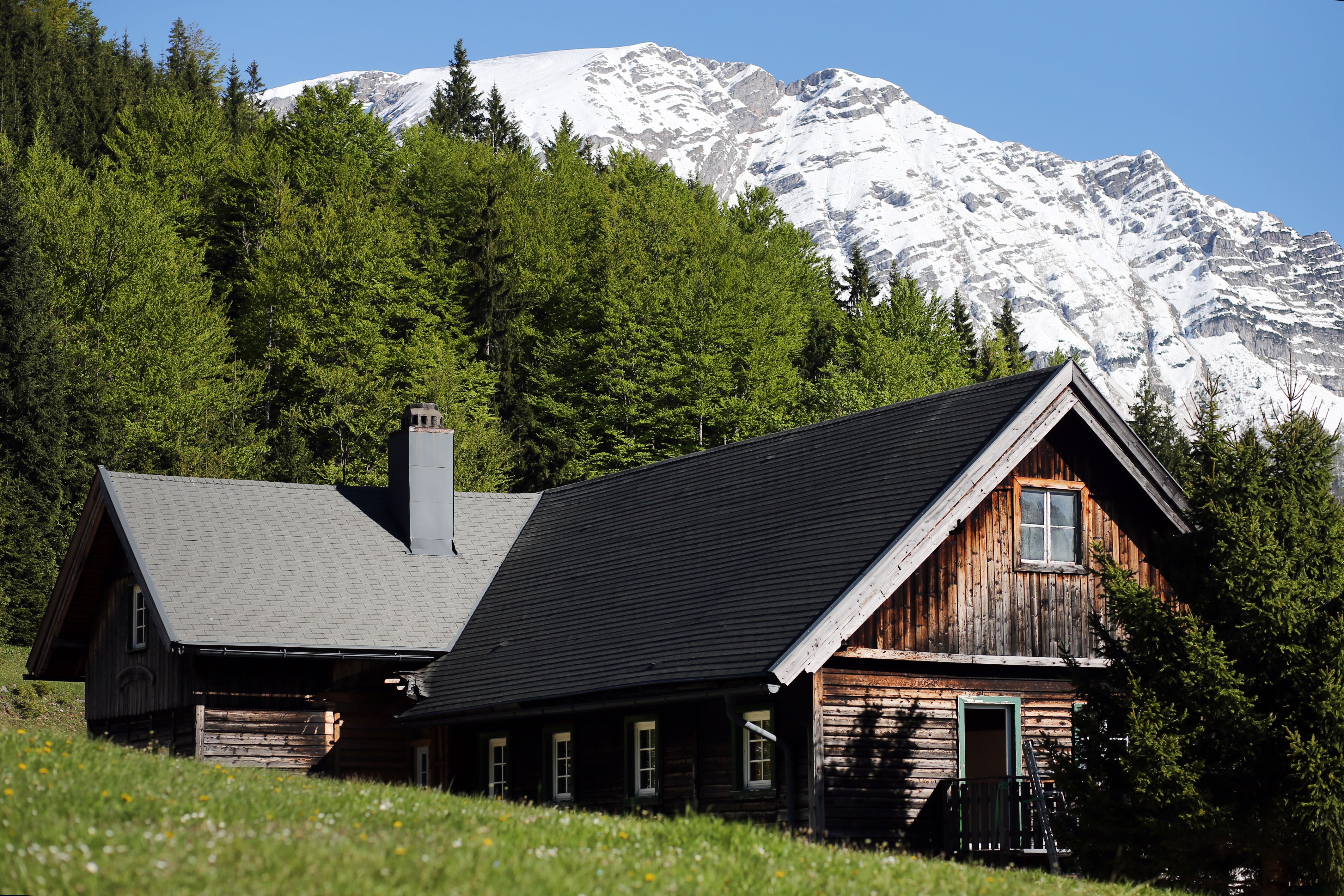 Holzhütte vor schneebedecktem Berg und grünem Wald.