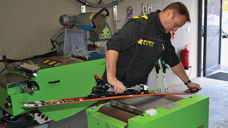 Mitarbeiter bearbeitet einen Ski mit einer Servicemaschine in einer Werkstatt.