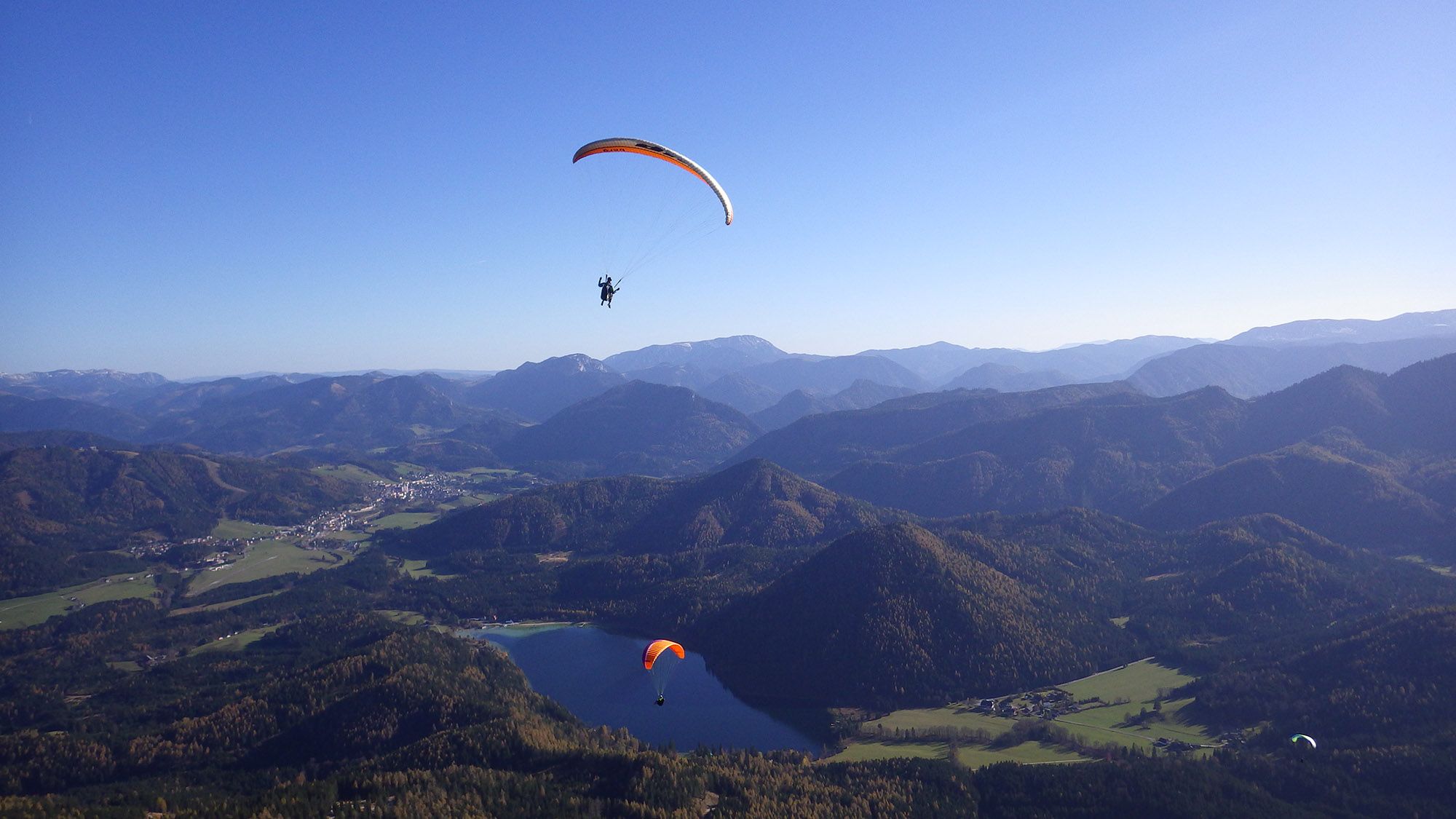 Drei Paragleiter schweben über dem Erlaufsee und der umliegenden Berglandschaft.