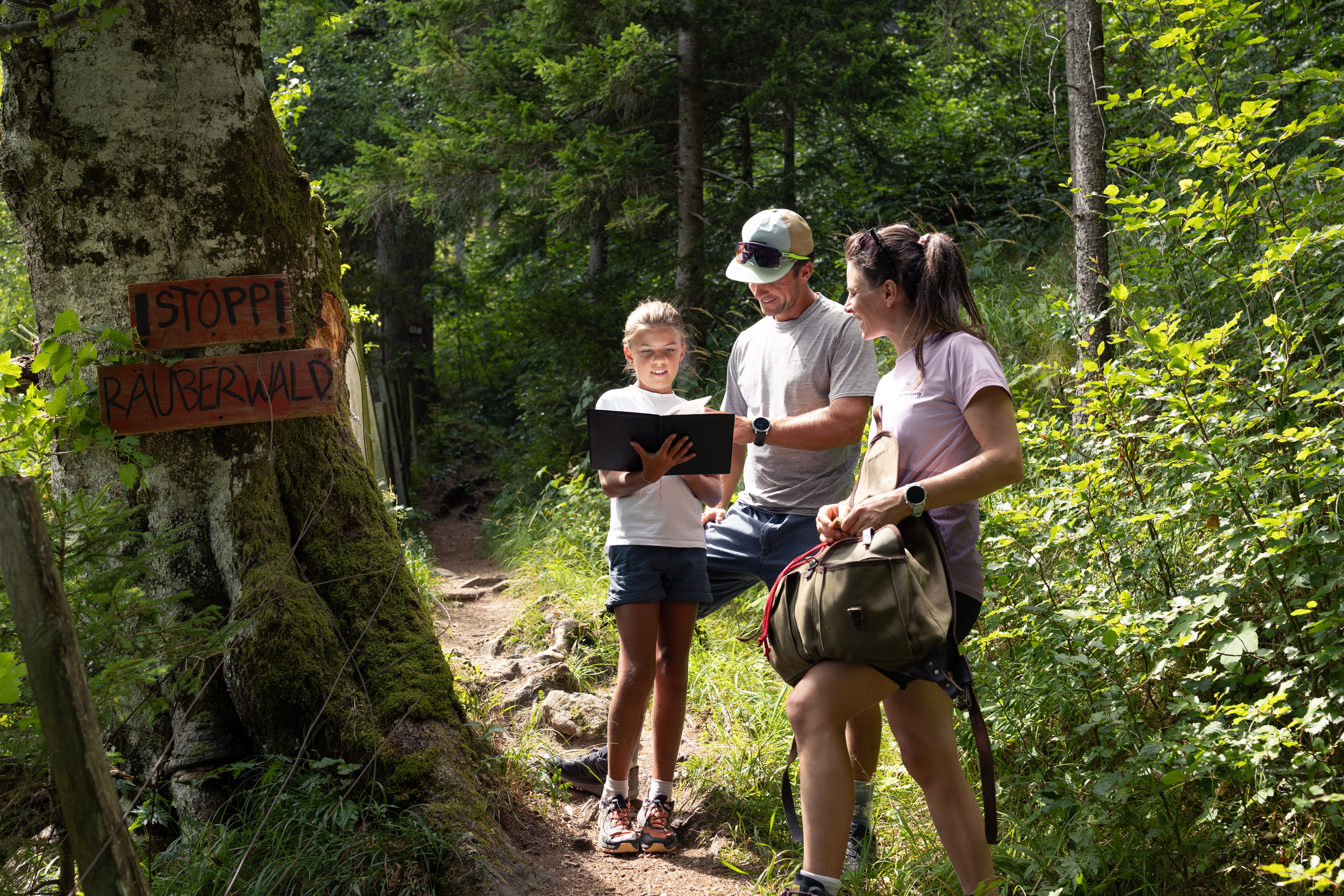 Mädchen löst mit zwei Erwachsenen eine Aufgabe an einer Station im Wald.