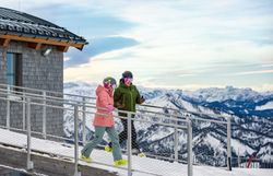 Ein Paar genießt einen romantischen Spaziergang auf der schneebedeckten Terrasse des Terzerhauses, umgeben von majestätischen Bergen. Die klare, kalte Luft und der atemberaubende Ausblick auf die winterliche Landschaft schaffen eine unvergessliche Atmosphäre für Skifahrer und Naturliebhaber.