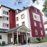 Au&szlig;enansicht eines mehrst&ouml;ckigen Geb&auml;udes mit roter und wei&szlig;er Fassade, beschriftet mit "Zusers Pension".