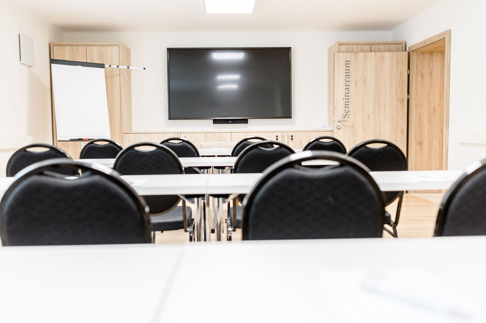 Ein moderner Seminarraum mit Stühlen, Tischen, einem großen Bildschirm und einem Flipchart.