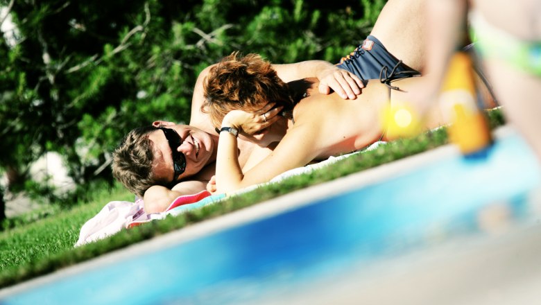 A couple relaxes on a lawn by the pool at the Mitterbach outdoor pool.