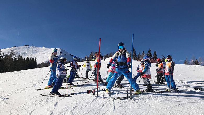 Skilehrkräfte üben mit mehreren Kindern zwischen Markierungsstangen auf einer verschneiten Piste.