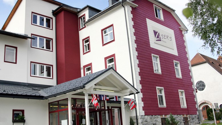 Zusers Pension - Außenansicht, © zVg Außenansicht eines mehrstöckigen Gebäudes mit roter und weißer Fassade, beschriftet mit "Zusers Pension".
