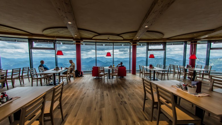 Innenansicht eines modernen Restaurants mit Panoramafenstern und Bergblick.