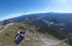 Mehrere Gleitschirmflieger &uuml;ber einem Berg mit Blick auf ein Tal und den Erlaufsee