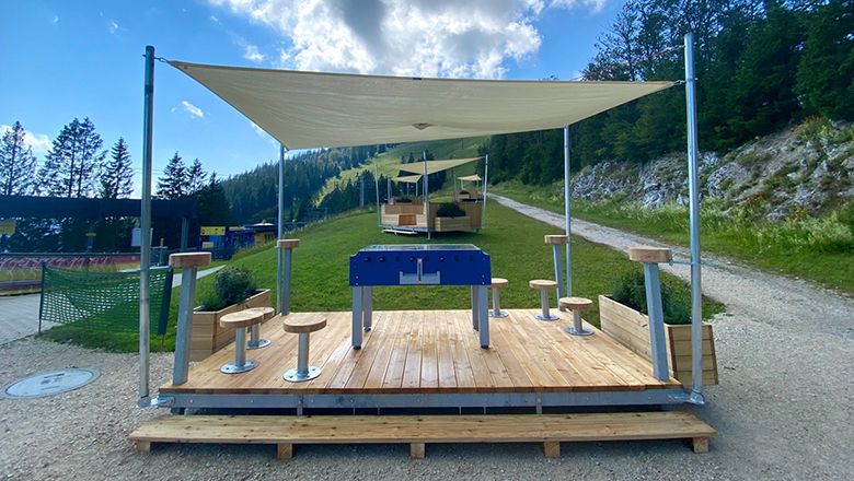 Überdachter Tischfußballplatz mit Sitzhockern an einem Berghang.