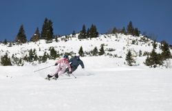 Zwei Skifahrende ziehen auf einer breiten Piste parallel durch den Schnee.